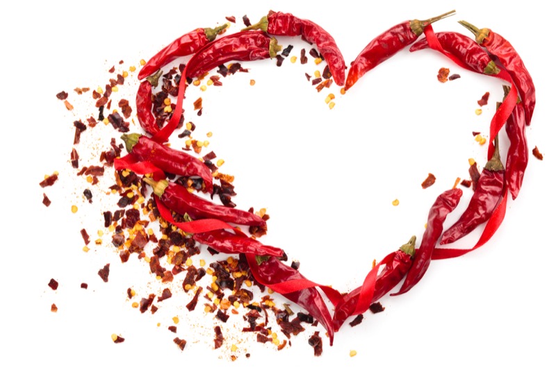 Heart of chili peppers and red ribbon isolated on white background.