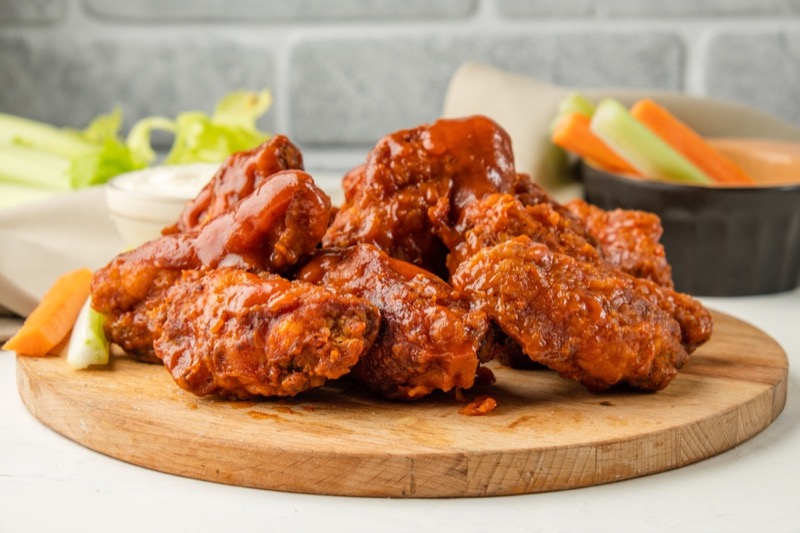 Appetizing fried buffalo chicken wings served on a wooden board with vegetables on the background