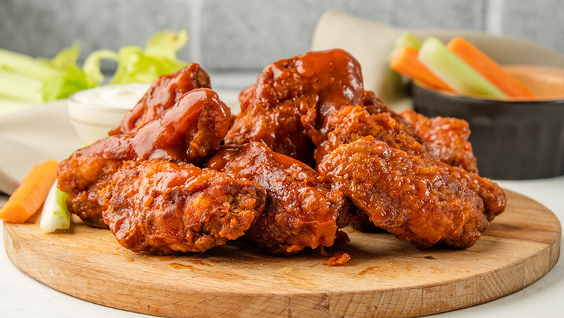 Appetizing fried buffalo chicken wings served on a wooden board with vegetables on the background.